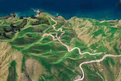 Aerial view of green hills and ocean, winding roads on the mountain top in New Zealand , white road lines, photorealistic landscapes, aerial photography, aerial view, photorealism, natural light, hyper realistic --ar 128:85