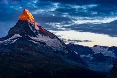 A breathtaking view of the iconic peak of The Matterhorn mountain in Zermatt, Switzerland at dawn with a dramatic sky. High resolution photography with detailed and intricate compositions in a perfect composition with golden hour lighting and professional color grading and depth of field, shot on a Sony Alpha A7 III camera. --ar 128:85