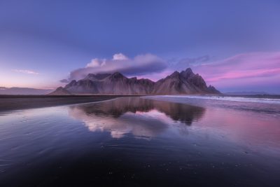 Vestrahorn mountain in Iceland, black sand beach, pink and purple sky, sunset, long exposure photography, rule of thirds composition, reflection on the ground, wide angle shot, Nikon D850, 24mm lens, f/9, ISO 64, natural light, landscape photography, --ar 128:85