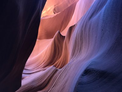 A photograph of an abstract canyon, where the walls and ground form beautiful patterns that create the illusion of water in motion. The colors are warm with shades of orange, pink, blue, and purple. It is illuminated with soft sunlight that casts shadows on the wall, creating a play between light and dark. This photo was taken using a Canon EOS R5 camera and EF lens at f/28, capturing every detail of textures and shapes in the style of soft sunlight. --ar 4:3