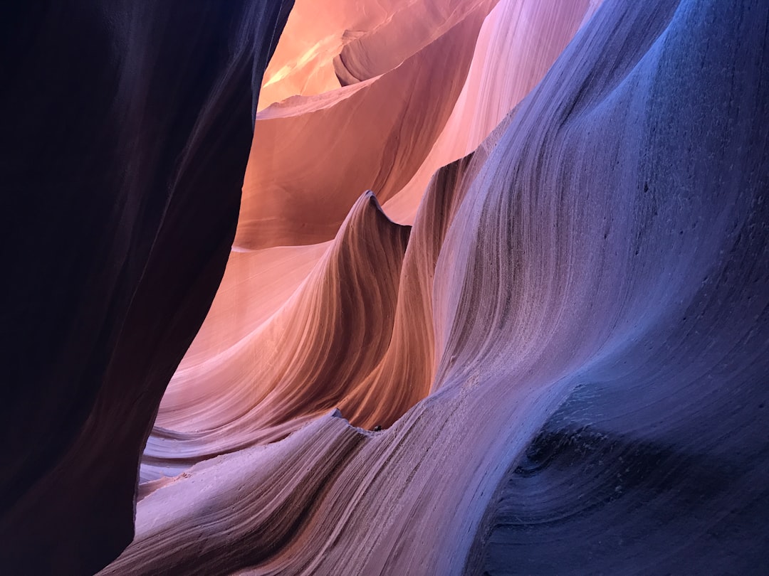 A photograph of an abstract canyon, where the walls and ground form beautiful patterns that create the illusion of water in motion. The colors are warm with shades of orange, pink, blue, and purple. It is illuminated with soft sunlight that casts shadows on the wall, creating a play between light and dark. This photo was taken using a Canon EOS R5 camera and EF lens at f/28, capturing every detail of textures and shapes in the style of soft sunlight. –ar 4:3