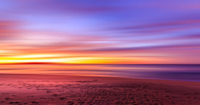 Beautiful colorful sunset on the beach with a beautiful sky and calm sea, long exposure photography using a wide angle lens, during the golden hour with soft lighting and vibrant colors, created a tranquil scene with a serene atmosphere on the sandy shore by the tranquil ocean on a sandy beige beach, with warm hues of orange, purple and blue in the sky. --ar 128:67