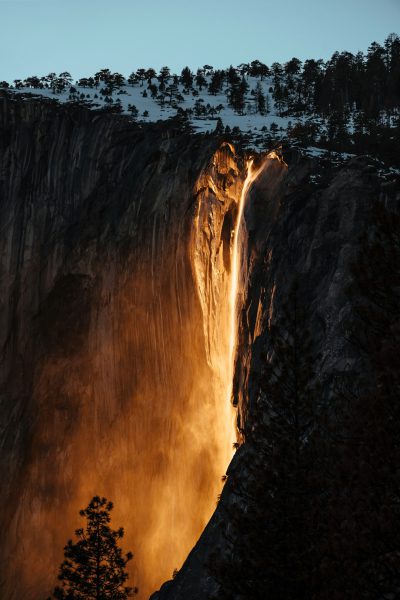 Ho adidas lighting, golden hour, long exposure, lights up the top of yosemite's fire fall in winter. the light from behind shines on an orange waterfall with trees at its base. photo taken in the style of daniel kordan, panoramic shot, dutch angle shot, golden color grading, clear and sharp focus, hyper realistic, high resolution, hyperrealistic --ar 85:128