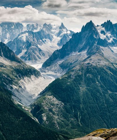 photo of the chailles mountains in france, with snowcapped peaks and glaciers in summer. shot from high up on one mountain peak overlooking another, with green forest below. --ar 107:128