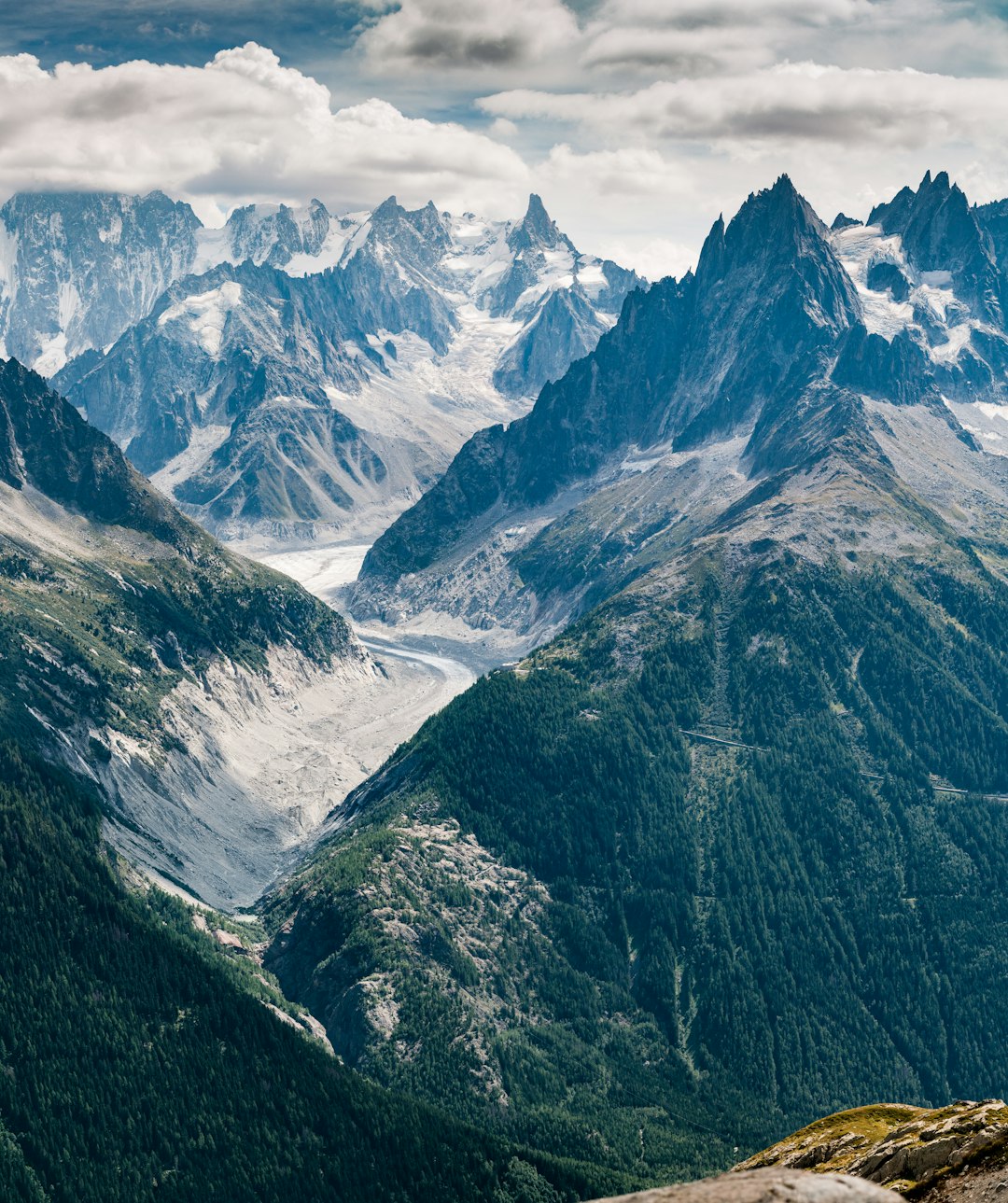 photo of the chailles mountains in france, with snowcapped peaks and glaciers in summer. shot from high up on one mountain peak overlooking another, with green forest below. –ar 107:128