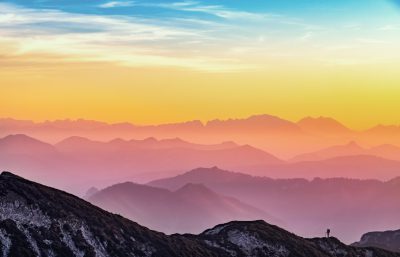 Beautiful panoramic view of mountains at sunrise with silhouette of hiker in the foreground. Aerial view of colorful sky and layers of mountain range in the background. Isolated on pastel background, real photo, photography in the style of 8k. --ar 64:41