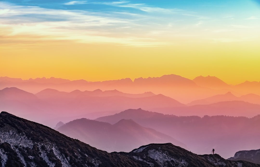 Beautiful panoramic view of mountains at sunrise with silhouette of hiker in the foreground. Aerial view of colorful sky and layers of mountain range in the background. Isolated on pastel background, real photo, photography in the style of 8k. –ar 64:41