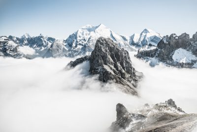 A view of the mountain peaks in Italy, from above surrounded by clouds, on top there is an isolated rock with snow and ice. The photograph was taken using a Sony Alpha A7 III camera with a wideangle lens at an F/8 aperture setting and ISO speed set to 400 for good exposure. The scene has a high resolution and is in full focus, showing every detail of the landscape. --ar 128:85