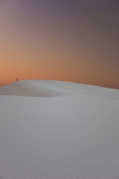 A lone figure standing atop the white sand dunes of Whitehandory, New Mexico at dusk with a gradient sky from orange to purple, creating an atmosphere of solitude and contemplation, Photography, using a wideangle lens for panoramic views, --ar 85:128