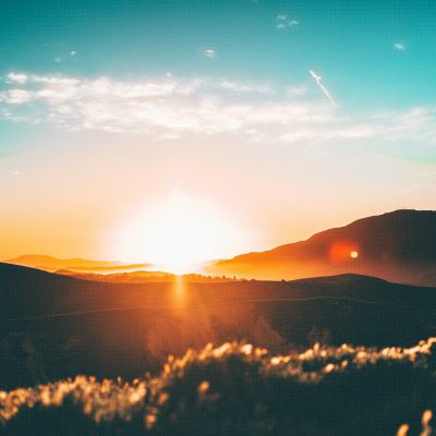 Sunset over the mountains, photo with a blurred background, bright sky and sun in the foreground, grainy film filter giving warm colors, golden hour lighting, landscape photography of greenery and desert, nature photography with a panoramic view, cinematic and beautiful picturesque scene, sunrise with orange and blue tones, sunny day in summer, desert mountains in the distance, grass on the ground, bokeh effect with depth of field using a wide angle lens, shot with a Sony Alpha A7 III camera in the style of landscape photography.