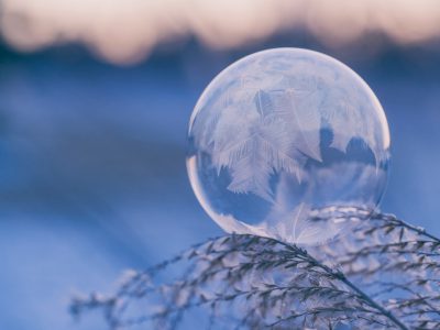 A closeup photo of an ice-covered soap bubble, reflecting the winter landscape in soft pastel hues. The background is blurred to emphasize the crystallized sphere, with delicate frost patterns on its surface. In sharp focus, frozen grasses add texture and depth to the scene. --ar 4:3