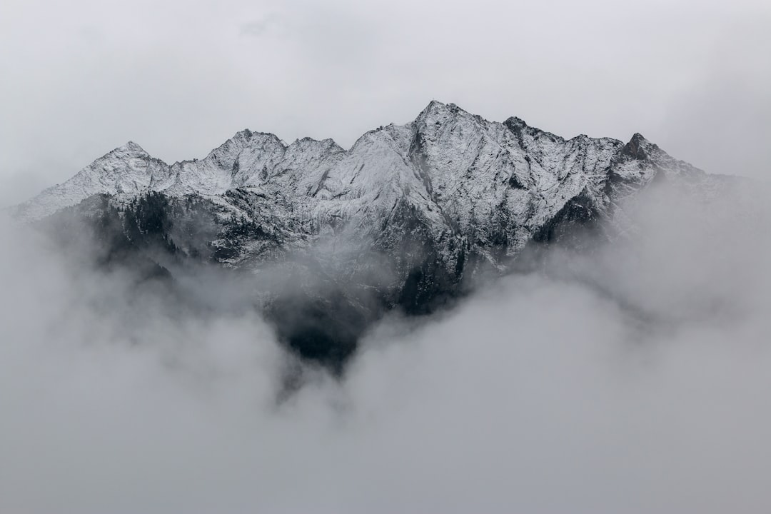 A snow-covered mountain range partially obscured by low clouds, creating an ethereal and mysterious atmosphere. The peaks stand tall against the grey sky, adding depth to the scene. Shot with a Canon EOS R5 camera using a wide-angle lens at f/8 for a dramatic effect. –ar 128:85