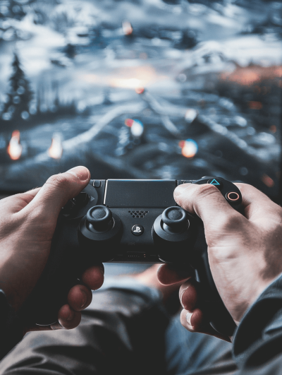 A person holding a game controller while playing on a console in front view, with a background showing video games and gaming elements. The focus is on their hands as they play the game. The style should be in the style of realistic photography, capturing detailed textures like textured skin, realistic lighting, and realistic reflections. Use a Sony A7 III camera to capture high-resolution details. Ensure that both sides of his hands can be clearly seen.